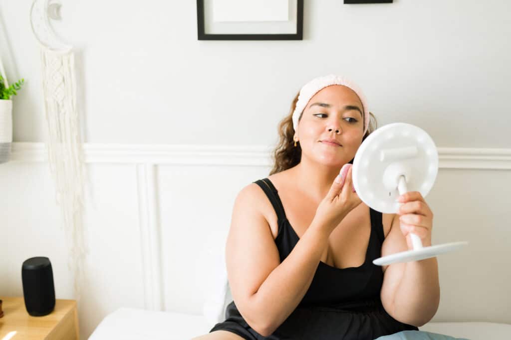 Woman getting ready to go out applies makeup to conceal acne scars on her face.